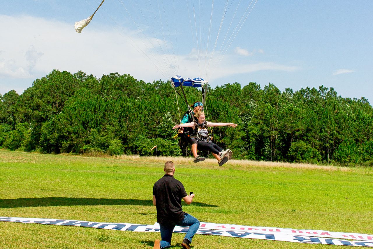 Young female comes in for landing from tandem skydive and sees will you marry me banner laid out in the grass