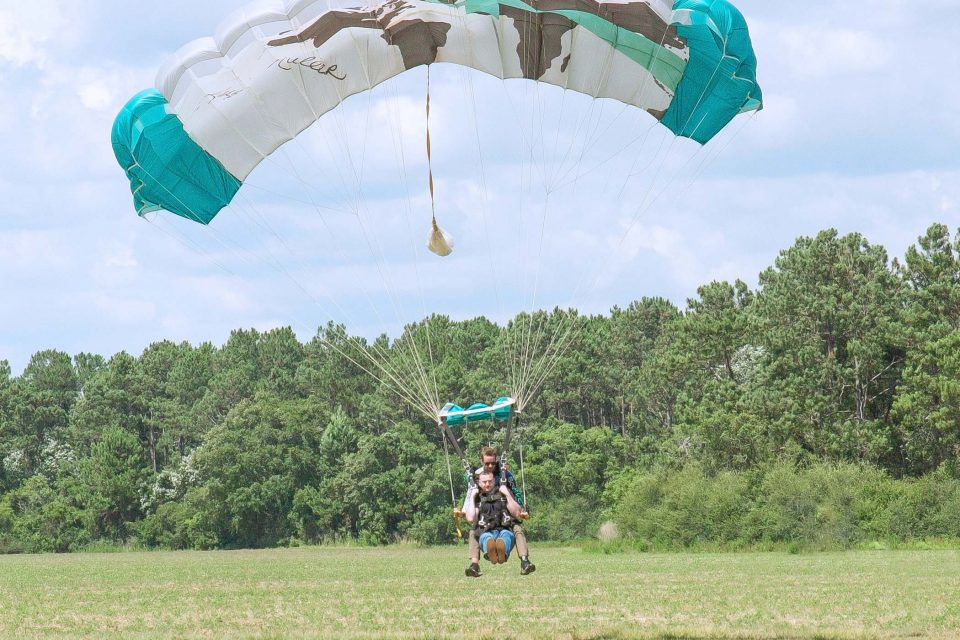 man holds his legs up as he comes in for landing from a skydive with the skydive the gulf tandem instructor
