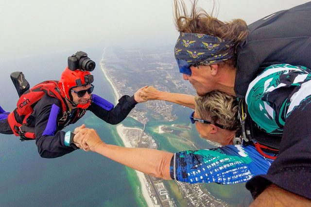 tandem skydiver and videographer holding hands during free fall portion over the ocean skydive